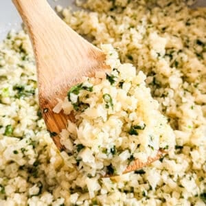 A close up image of a wooden spoon holding a scoop of cilantro clime cauliflower rice.