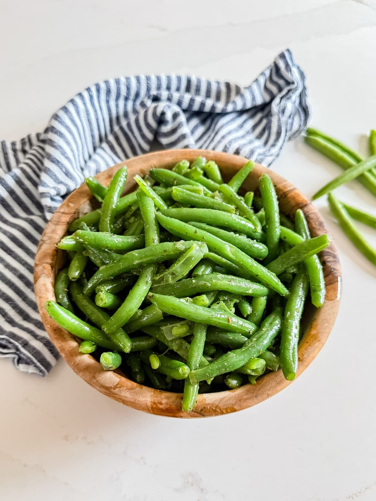 A wooden bowl of green bean salad with a striped towel in the background.
