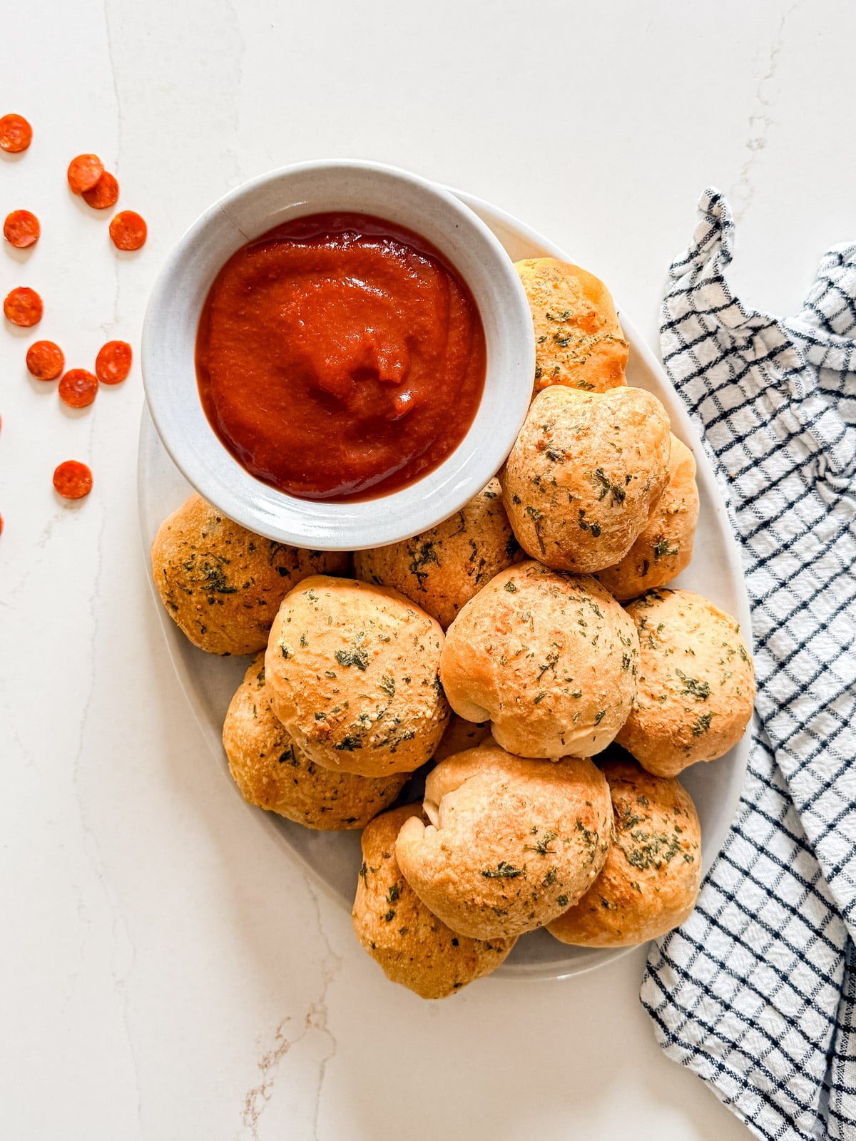 An overhead image of a plate of mini pizza bites with a bowl of pizza sauce.