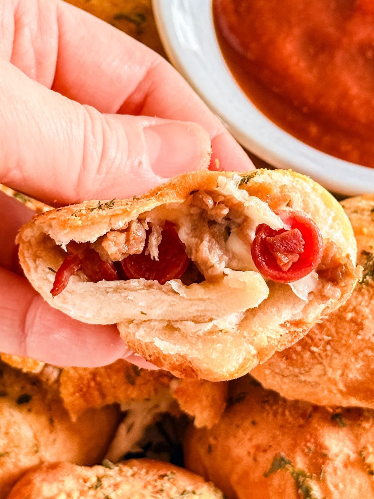 A hand holding a pizza bite that's cut in half revealing the cheesy, meaty filling.