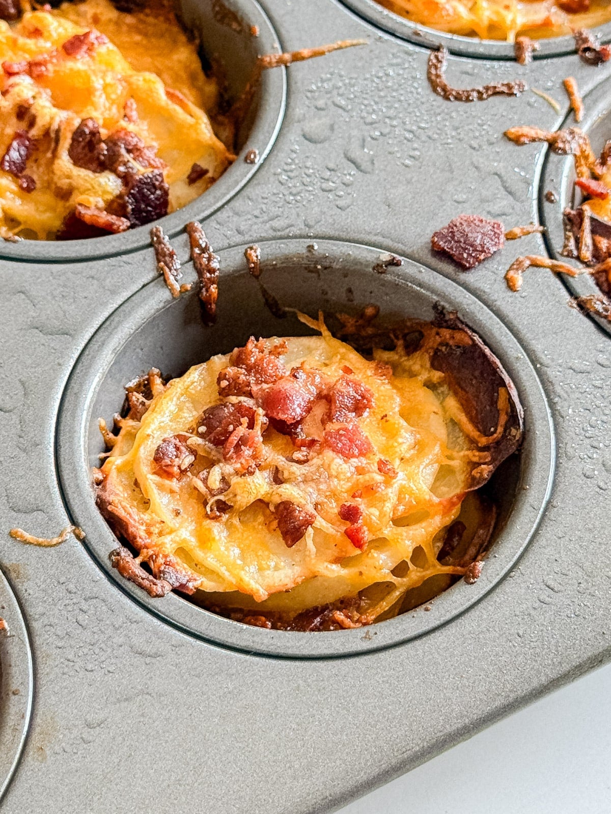 A close up of a potato stack in a muffin tin with cheese and bacon.