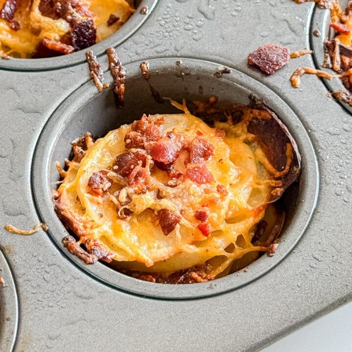 A close up of a potato stack in a muffin tin with cheese and bacon.
