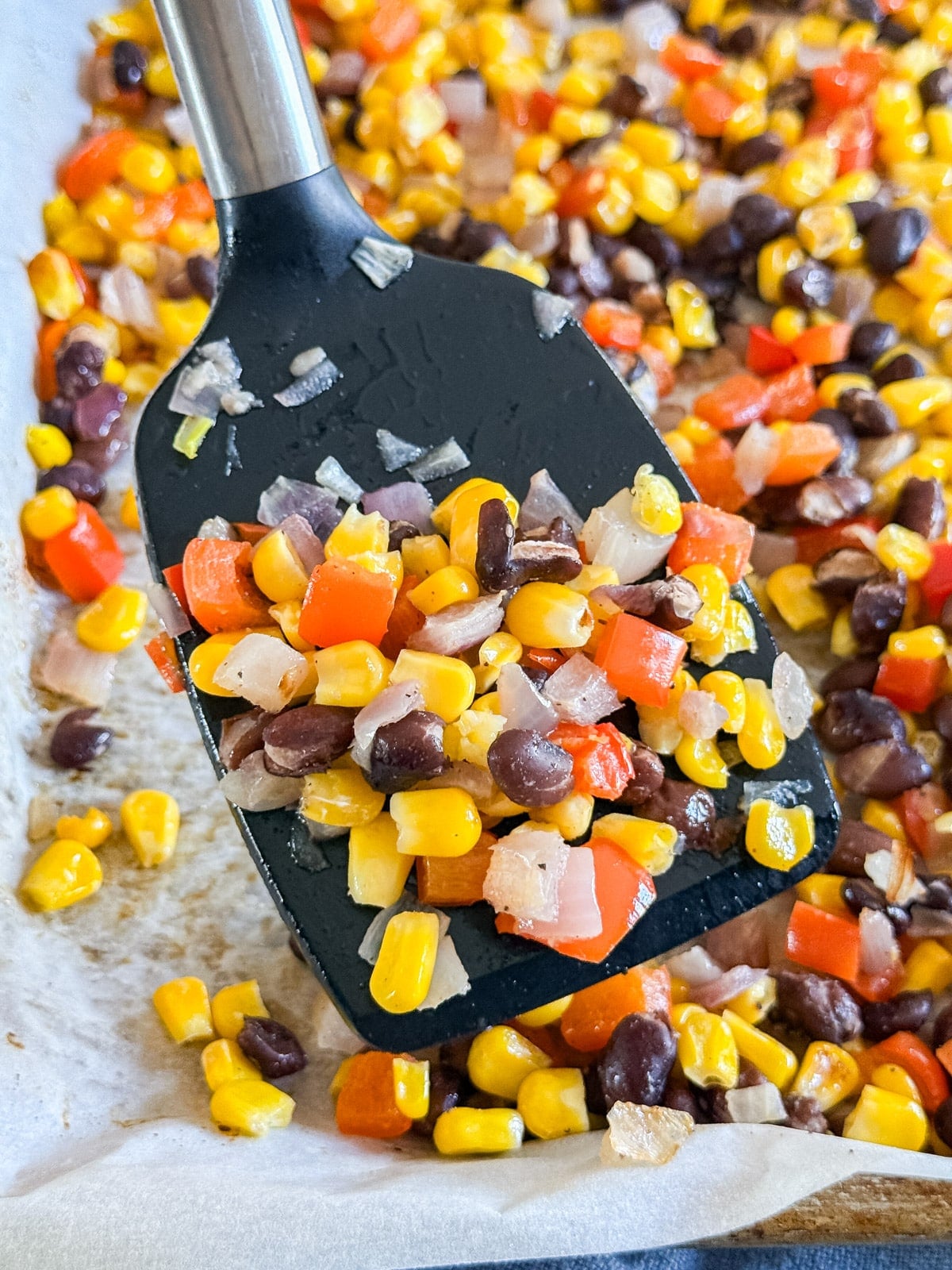A spatula holding corn salsa up close to the camera from the pan.