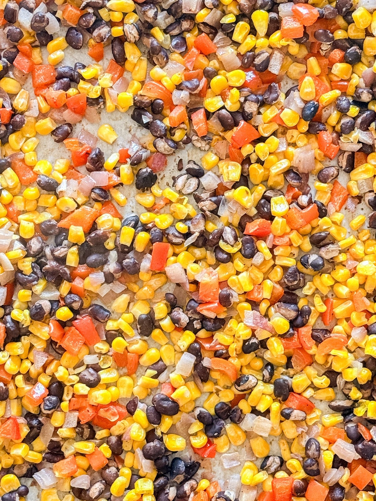 A close up overhead image of corn salsa spread out on the sheet pan.