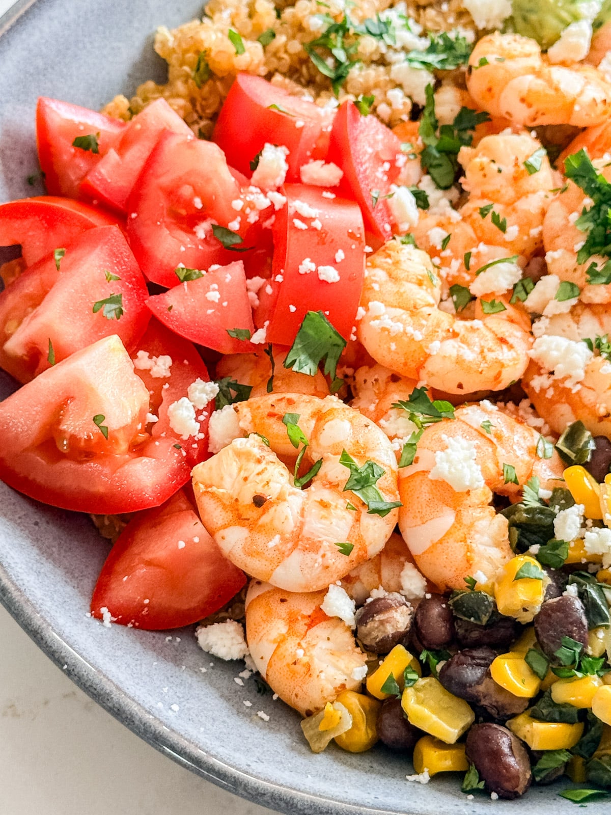 A close up image of the shrimp, tomatoes and corn salsa on a quinoa bowl.