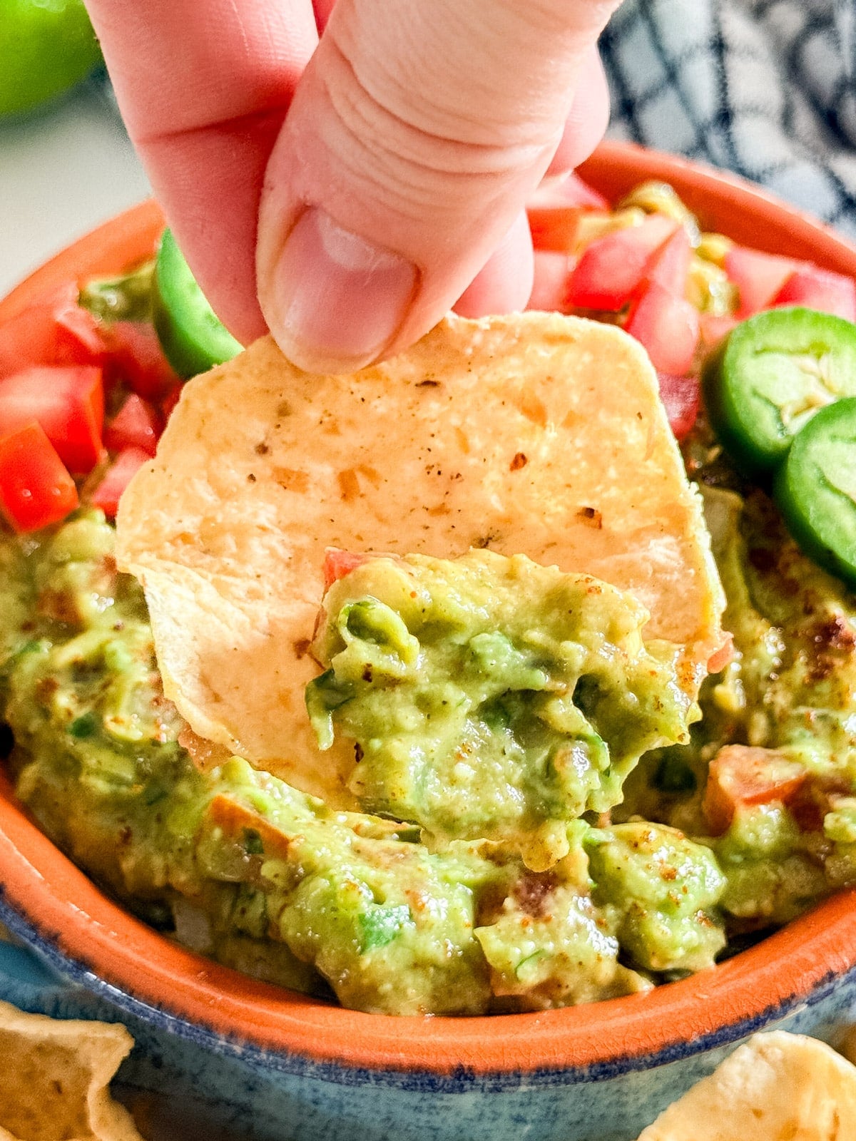 A close up image of a hand pulling a chip with guacamole out of the bowl.