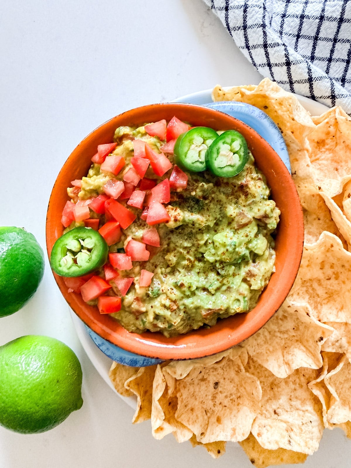An overhead image of a bowl of guacamole next to chips and limes