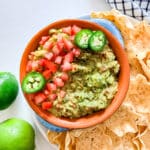 An overhead image of a bowl of guacamole next to chips and limes