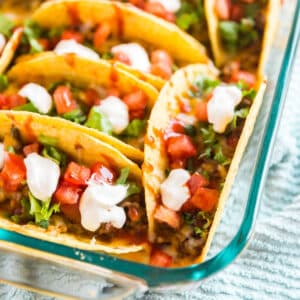 The corner of a baking dish with baked tacos in it.