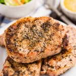 A plate with herb grilled pork chops stacked on it.