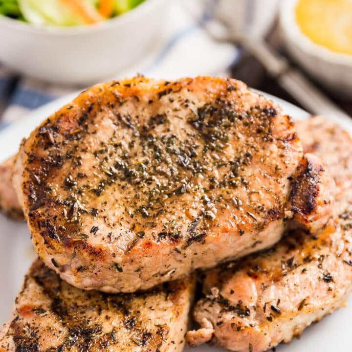 A plate with herb grilled pork chops stacked on it.