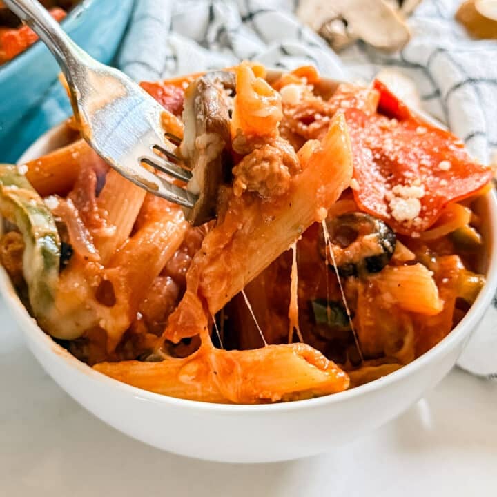 A fork pulling up a scoop of pizza pasta from a bowl.