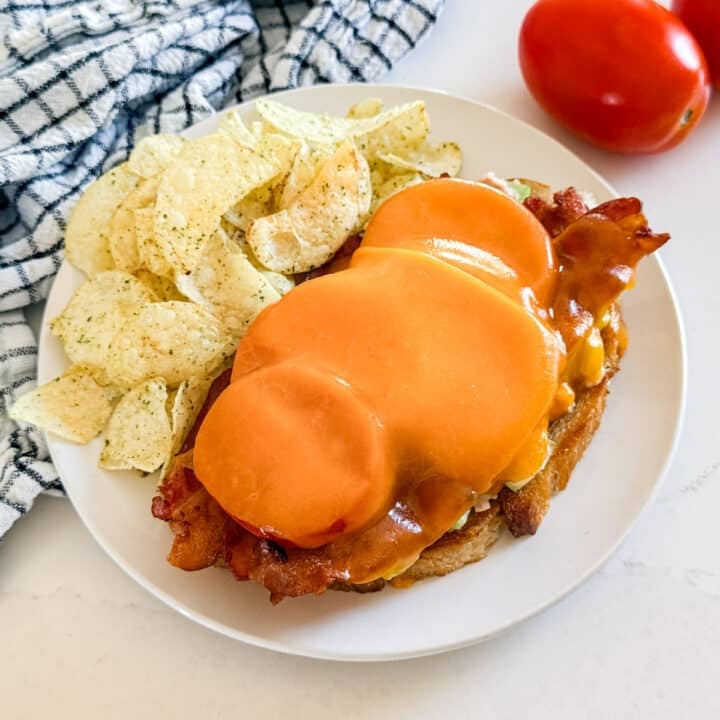 An open-faced tuna melt on a plate with chips.