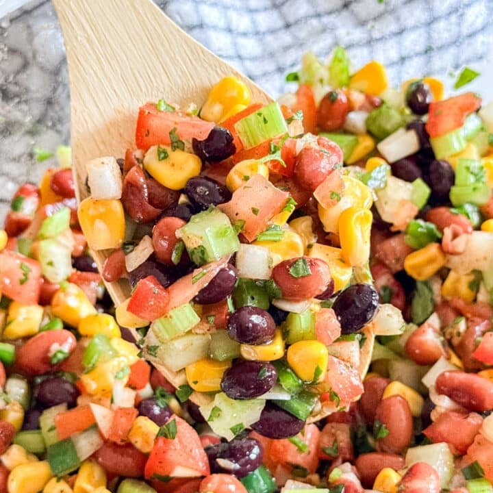 A wooden spoon holding a scoop of Mexican bean salad.