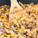 A wooden spoon in a pan of hamburger stew.