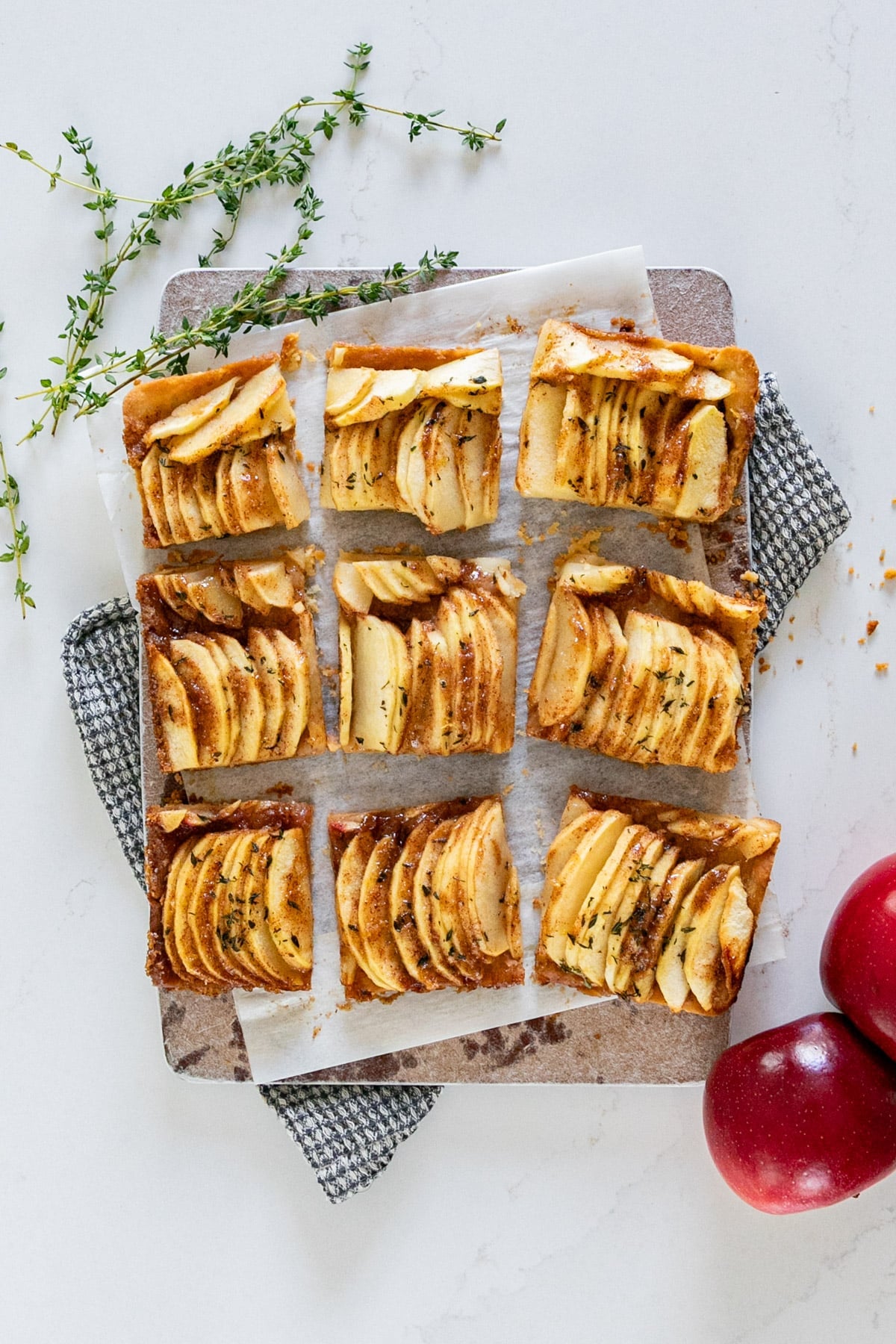 An overhead image of apple shortbread bars with thyme and apples around it.