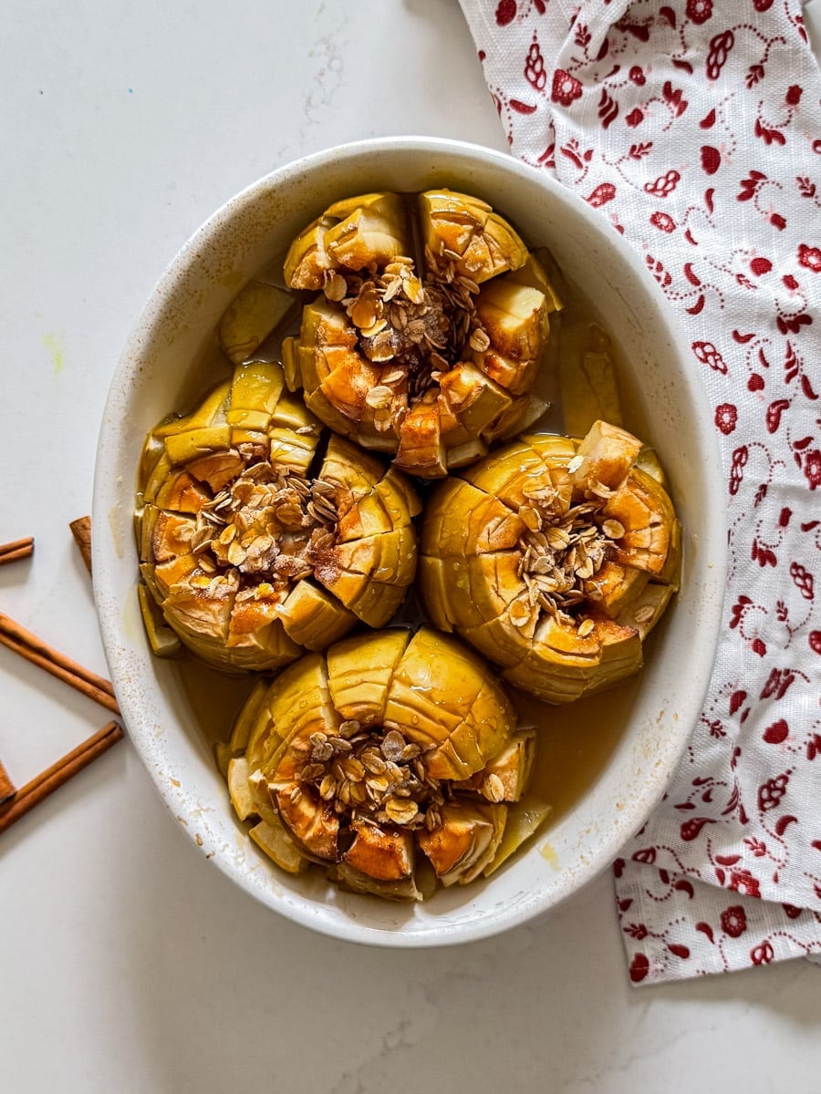 An overhead image of baked apples in a pan with a napkin and cinnamon sticks around it.
