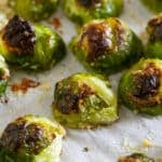 A close up of roasted Brussels Sprouts on a lined sheet pan.